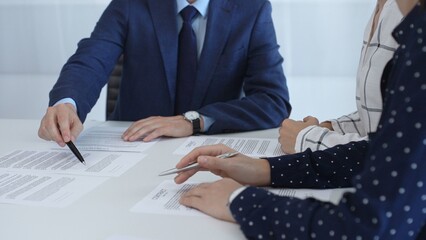 Business professionals analyzing contract details, gesturing with pens while discussing legal terms during collaborative meeting, focused on negotiation process