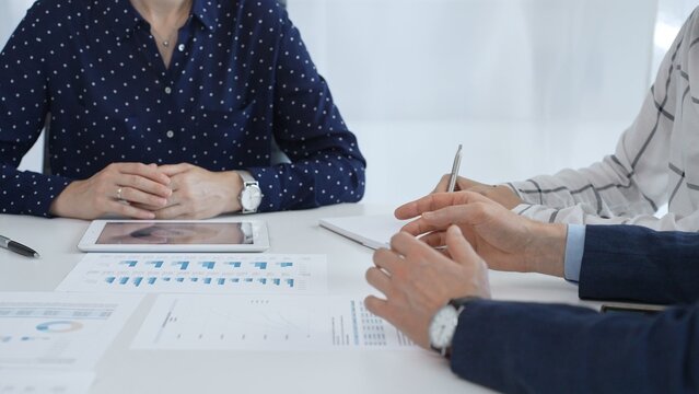 Professional colleagues examining financial documents, studying performance charts on paper and digital tablet during collaborative meeting in modern workplace setting