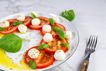 Caprese salad with tomatoes, mozzarella cheese and basil on a white plate