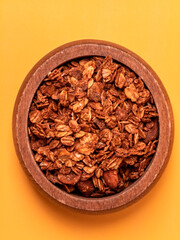 Top view of homemade granola in a wooden bowl on a yellow background