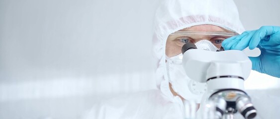 Professional scientist in protective gear is using microscope in a laboratory setting, close-up. Science and medicine concepts