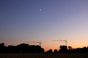Crescent moon and construction cranes at dusk
