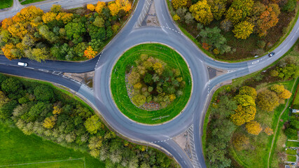 Aerial drone view of a road roundabout surrounded by colorful autumn foliage in the UK