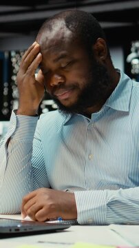 Vertical Video Black troubled worker rubbing his head in frustration and weariness, expressing fatigue and discomfort due to intense workload or failure. Angry frustrated man feels under pressure