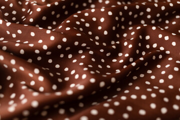Close-up of terracotta colored silk fabric with white polka dots, softly draped to create an abstract background. Copy space © DariaR