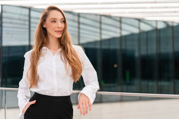 Smiling young businesswoman looking away with confidence. Lady with long brown hair in formals standing outside office building during daytime