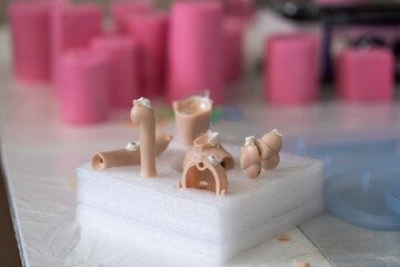 Closeup of silicone doll parts on foam base during the making process. Pink silicone molds and doll pieces are visible showing detailed crafting process in workshop setting