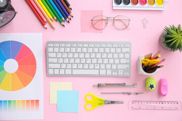 Workplace of graphic designer with keyboard, color charts and stationery on pink background