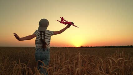 Child girl plays with toy airplane. Happy teenager runs with toy airplane through wheat field in sun. Child aviator dreams of fly becoming pilot. Little girl dreams of traveling as pilot. Slow motion.