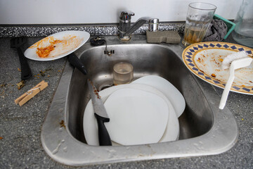 A messy kitchen sink is filled with dirty dishes, food scraps, and used utensils, indicating a need for cleaning.