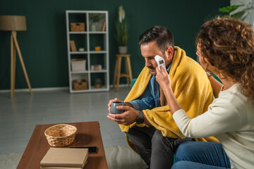 Woman checking sick man's temperature with a digital thermometer