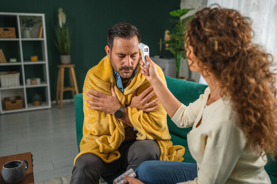 Woman checking ill man's fever with thermometer at home