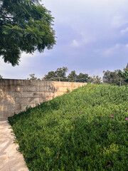 Minimal urban landscape with green slope and stone wall under cloudy sky