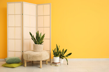 Stylish interior of room with sansevieria plants, folding screen and pouf near yellow wall