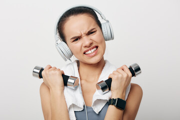 Young woman in activewear lifting small dumbbells with a determined grimace, wearing white...