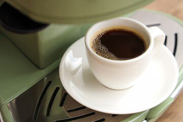 Modern coffee machine with cup of hot espresso in kitchen, closeup
