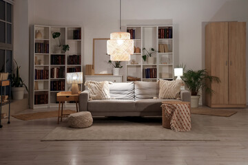 Interior of living room with sofa, glowing lamps and book shelves at night