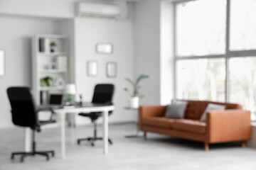 Blurred view of modern office with leather sofa and workplace near window