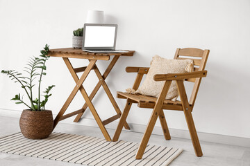 Interior of modern stylish room with chair and table with laptop near white wall