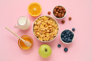 Bowl with cornflakes and ingredients on pink background