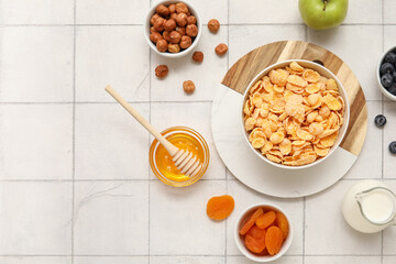 Bowls with cornflakes and ingredients on beige tile background