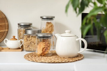 White teapot and jar with cookies on table in kitchen, closeup