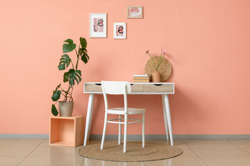 Comfortable workplace with houseplant, table and chair near coral wall in interior of room