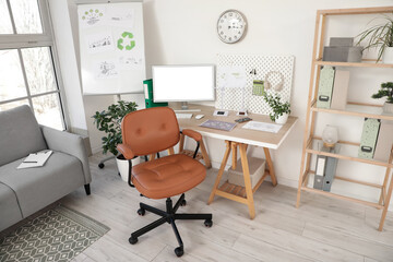 Brown swivel chair and workplace with modern computer near white wall in room
