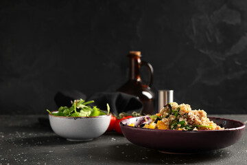 Bowl with healthy quinoa salad and ingredients on black speckled background