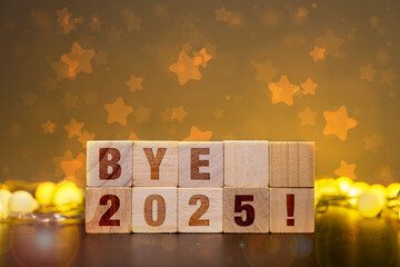 Wooden blocks spelling BYE 2025! with festive golden bokeh lights and star decorations, symbolizing...