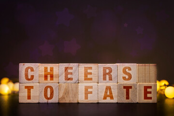 Cheers to Fate spelled out on wooden blocks with bokeh lights, celebrating destiny and future