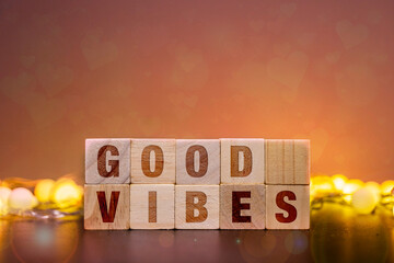 GOOD VIBES spelled out with wooden letter blocks, surrounded by warm glowing fairy lights on a dark surface with a bokeh heart background, symbolizing positivity and happiness.