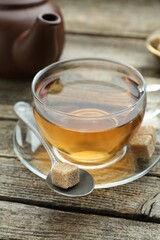 Aromatic black tea in glass cup, brown sugar and teapot on wooden table, closeup