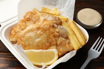 British Traditional Fish and chips with lemon and sauce on wooden table, closeup