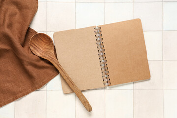 Blank recipe book with spoon and napkin on white tile background