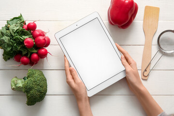 Female hands with digital recipe book, ingredients and kitchen utensils on white wooden background