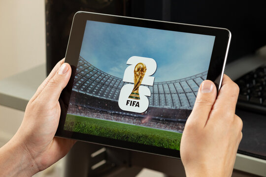 a male hands holding an iPad with the fifa world cup 2026 logo over a blurred stadium