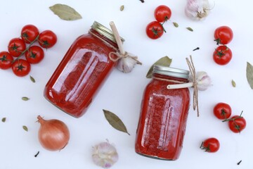 Tomato sauce, tomato paste, homemade, in jars on a white background, on the table, spices, twists for the winter
