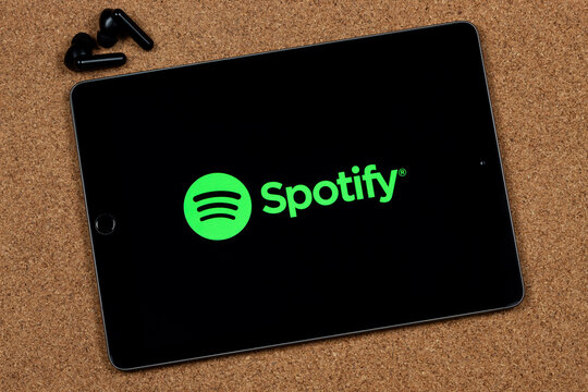 an iPad with the green spotify digital music logo with a black wireless earphones and a cork background