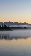 Fototapeta premium Serene mountain lake shrouded in morning mist with reflected sky and trees.