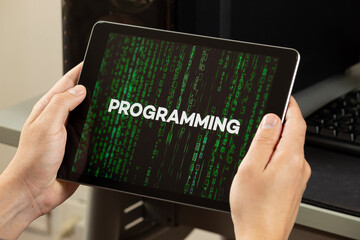 a male hands holding a tablet with the word programming over a green matrix code concept