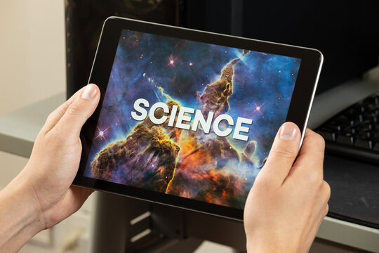 a male hands holding a digital tablet with the word science over a blurred nebula or galaxy