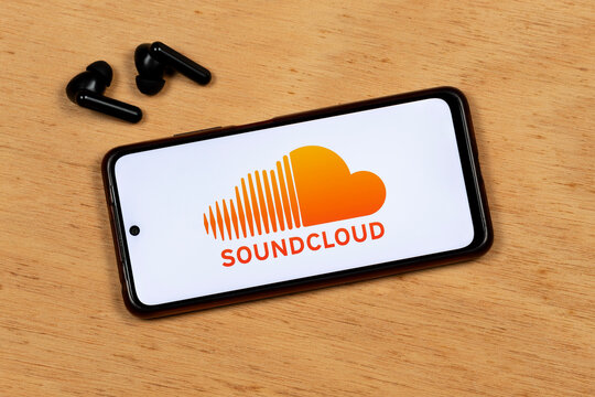 a smartphone screen showing soundcloud music streaming service orange logo with a wireless earphones over a wooden background