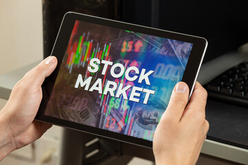 a male hands holding a tablet with the phrase stock market over a graph and chart concept