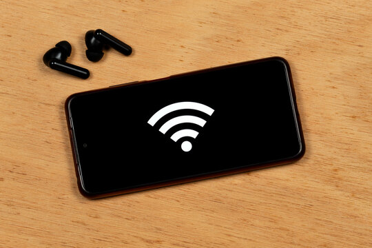 a smartphone with the white wifi symbol over a black color and a wireless earphones over a cork background