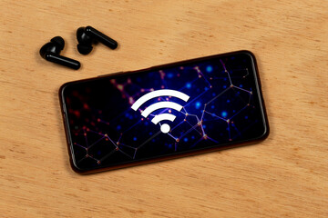 a smartphone with the white wifi symbol over a networking concept and a wireless earphones over a cork background