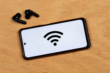 a smartphone with the black wifi symbol over a white worn out effect and a wireless earphones over a cork background