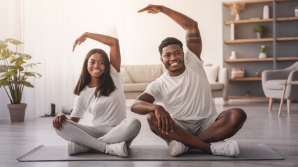Millennial black couple doing lateral flexion exercise, working out together at home sitting on floor mat. Happy young lady and her boyfriend making side bending pose in living room looking at camera