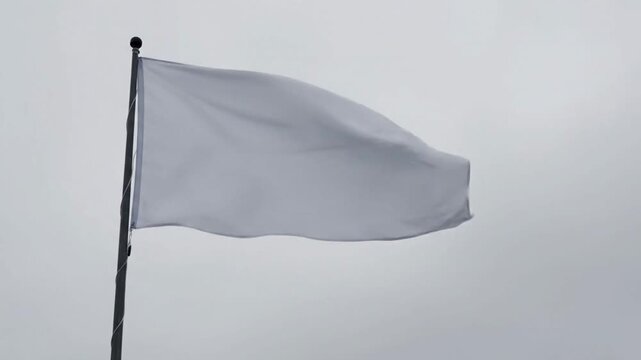 Waving White Flag Symbolizing Surrender Truce and Peace Against a Cloudy Grey Sky