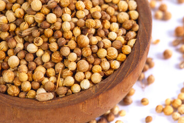 Top-down view of whole, dried coriander seeds in a rustic wooden bowl, isolated on a white background. An essential aromatic spice for cooking and culinary concepts.